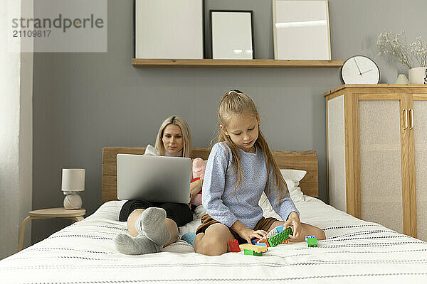 Daughter playing with blocks near mother at home