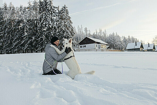 Affectionate man holding dog and kneeling in snow