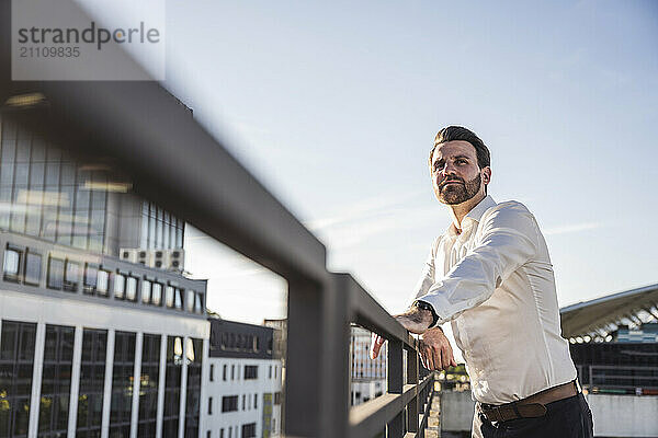 Contemplative businessman standing near railing on sunny day