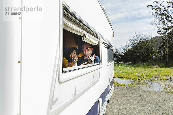 Smiling elderly couple with dogs near window of motor home