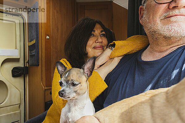 Happy senior woman leaning on man with dog in motor home