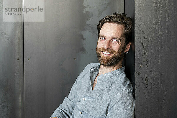 Happy businessman leaning on wall at office