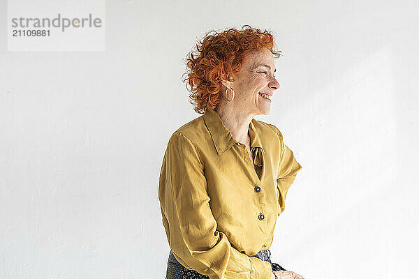 Smiling redhead woman sitting against white background