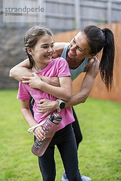 Happy woman embracing daughter standing in back yard