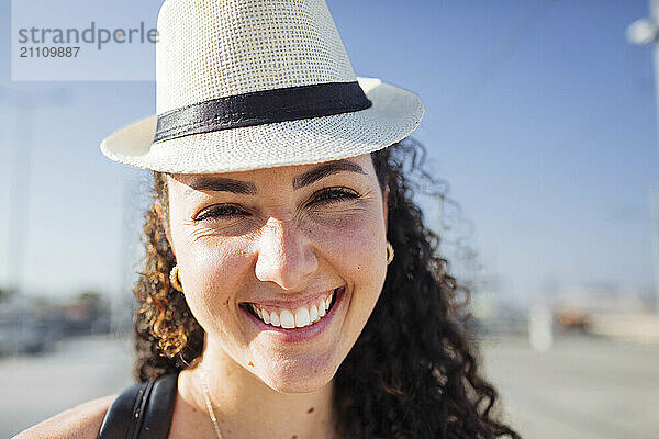 Smiling curly haired woman wearing hat on sunny day