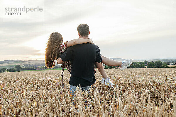 Young man carrying girlfriend amidst agricultural field