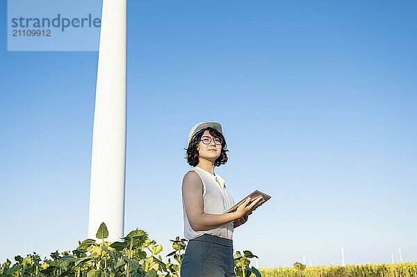 Young engineer holding tablet PC and standing at wind farm