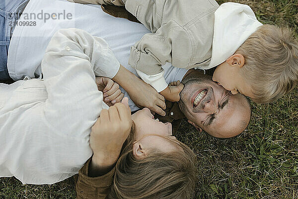 Boy kissing father lying beside woman at park