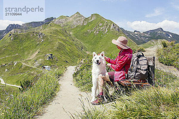 Mature woman resting on bench with dog in front of mountains