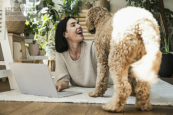 Smiling woman working on laptop near dog at home