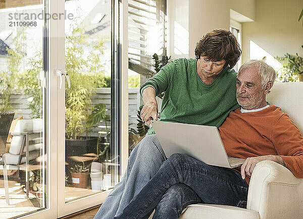 Senior couple sitting on chair and using laptop at home