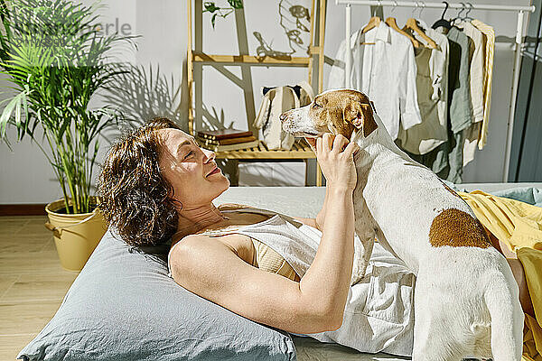 Woman petting Jack Russell Terrier dog on bed at home