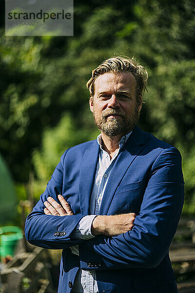 Mature businessman wearing blazer and standing with arms crossed at sunny day