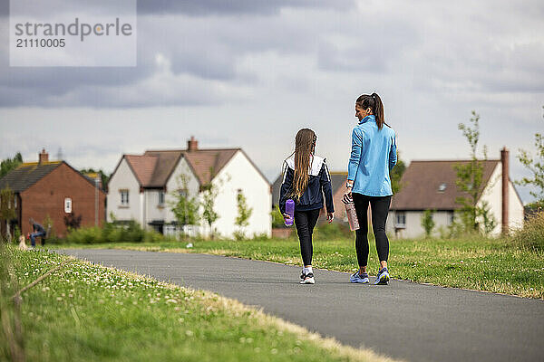 Mother and daughter walking on footpath near grass