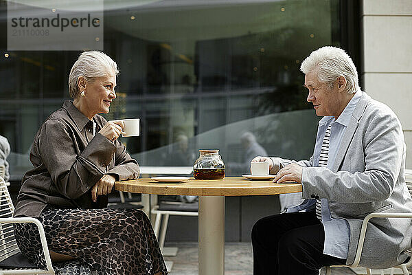 Senior couple sitting near table and drinking tea at outdoor cafe