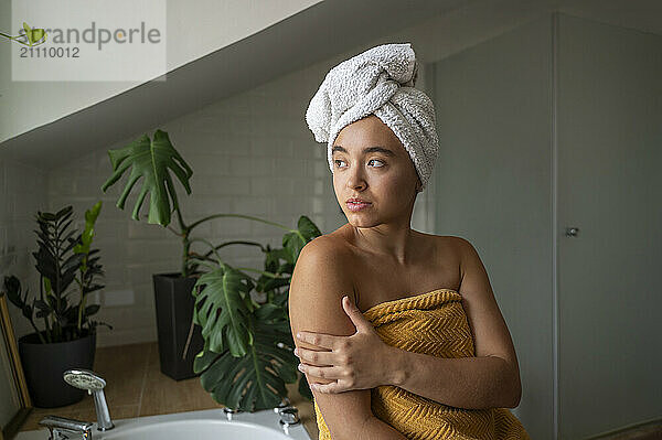 Contemplative woman wrapped in towel at bathroom