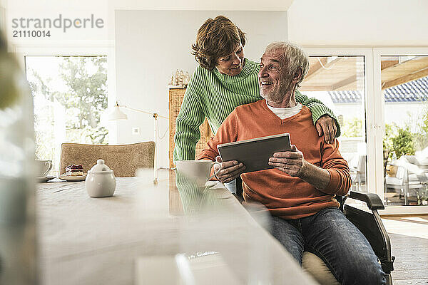 Senior woman with husband on wheelchair using tablet PC at home