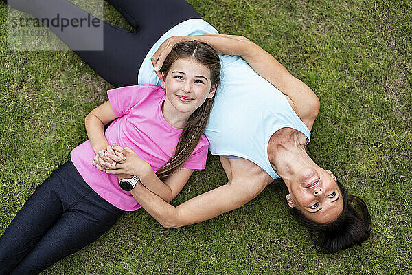 Smiling girl lying down with mother on grass in back yard