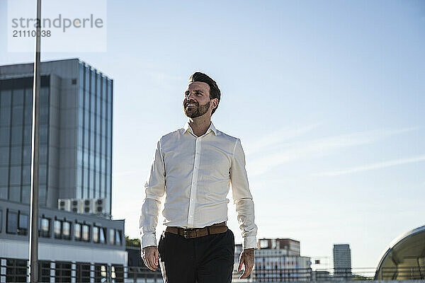 Happy businessman standing in front of sky on sunny day