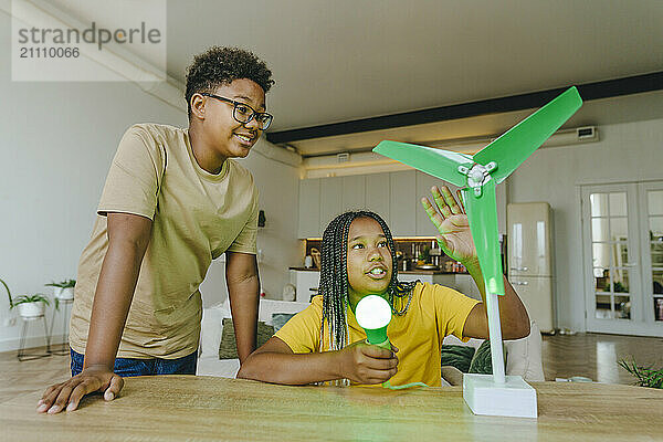 Siblings powering light bulb and discussing over wind turbine model at home