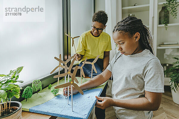 Brother and sister making wind turbines school project on window sill at home