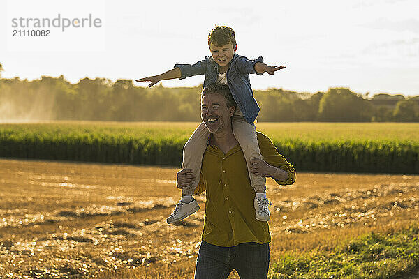 Happy boy with arms outstretched sitting on grandfather's shoulders