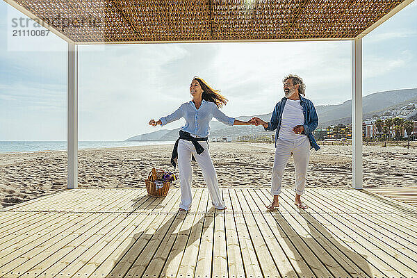 Happy senior man and woman holding hands while dancing at beach