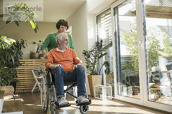 Senior woman pushing husband on wheelchair at home