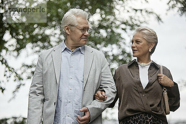 Senior man and woman standing arm in arm at street