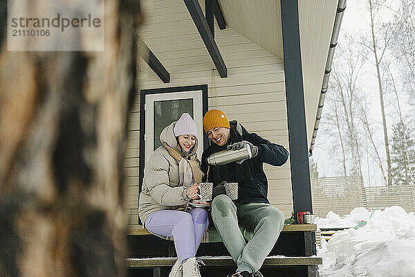 Smiling man serving hot coffee to woman sitting on porch