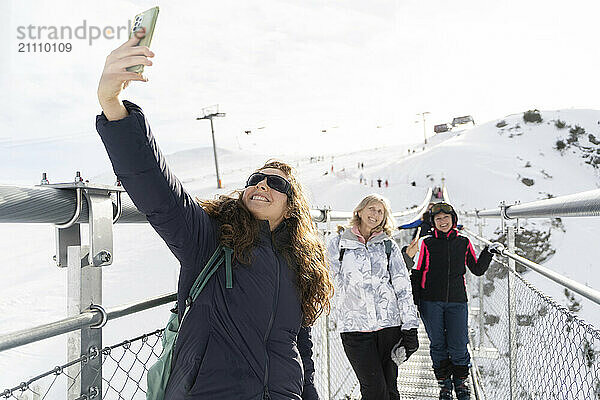 Happy woman taking selfie with friends through smart phone on bridge