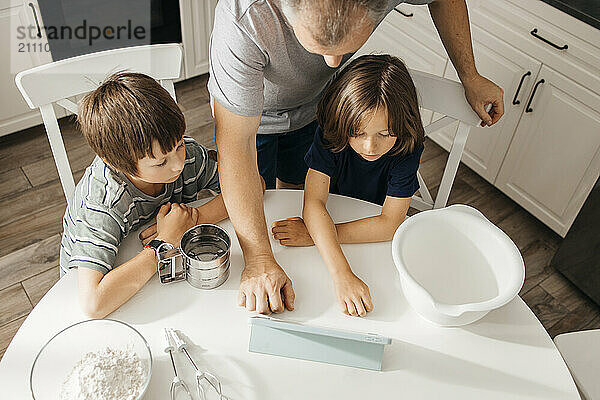 Father with children sitting near table and using digital PC in kitchen