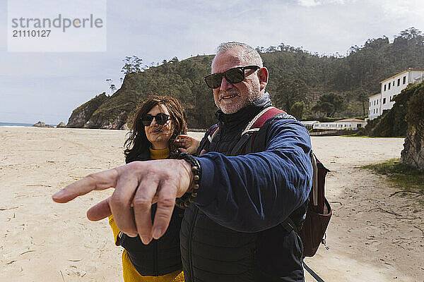 Senior woman with man standing and pointing at direction on beach