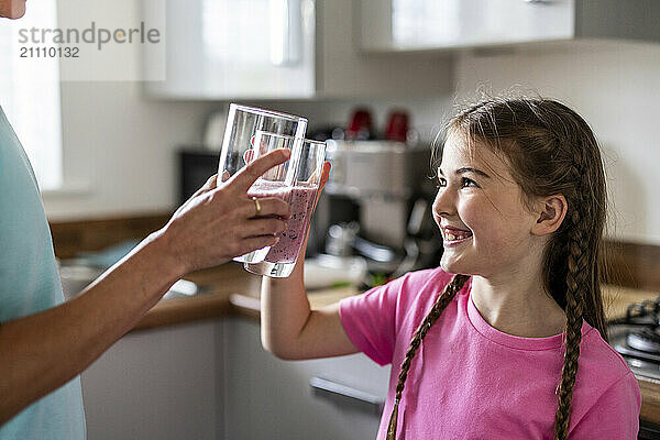 Happy girl toasting milkshake glass with mother at home