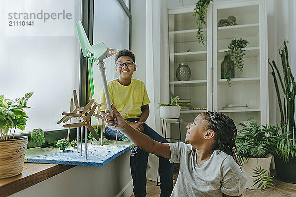 Happy siblings playing with toy wind turbines and making school project at home