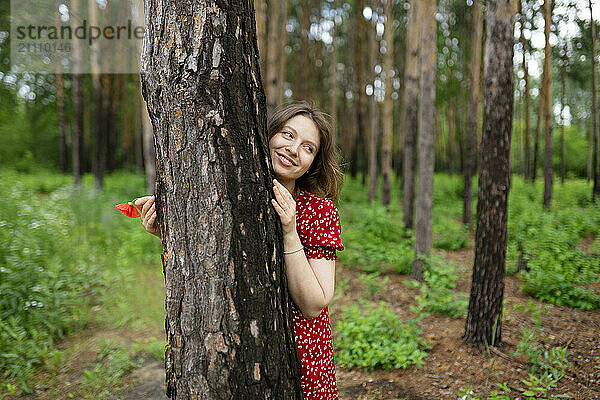 Smiling woman standing near tree trunk in forest