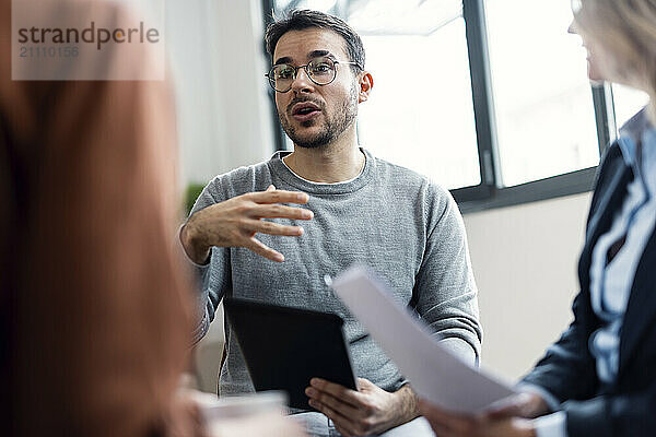 Businessman wearing eyeglasses explaining ideas to colleagues in office