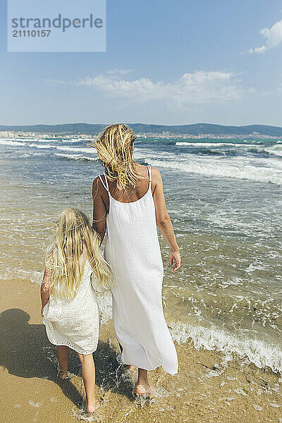 Mother and daughter walking at beach on sunny day