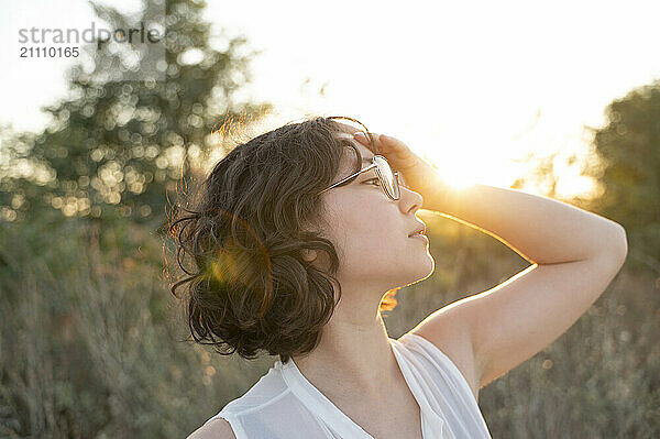 Woman with head in hand in field at sunset