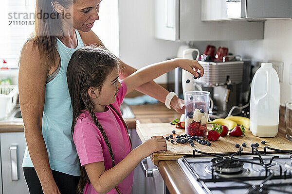 Girl helping mother in preparing milkshake at home