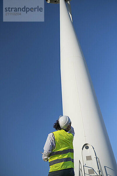 Engineer looking at wind turbine under blue sky