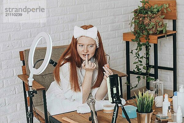 Teenage girl beauty blogger recording a makeup tutorial at home.