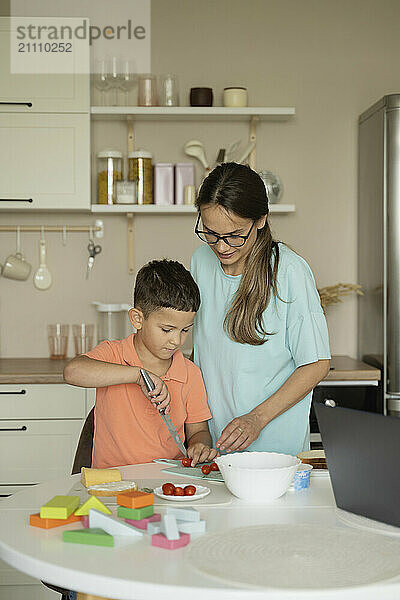 Son helping mother for cutting vegetable at kitchen