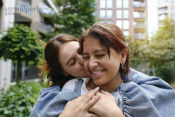 Young woman embracing and kissing girlfriend at park