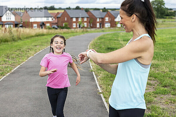 Woman timing daughter running on footpath