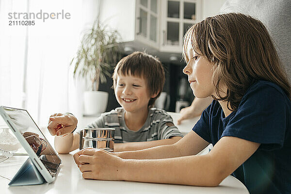 Siblings sitting near table and using digital PC in kitchen