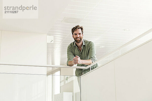 Smiling businessman leaning on railing at office