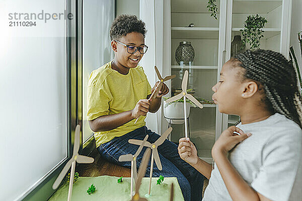 Smiling brother with sister blowing on toy wind turbines at home