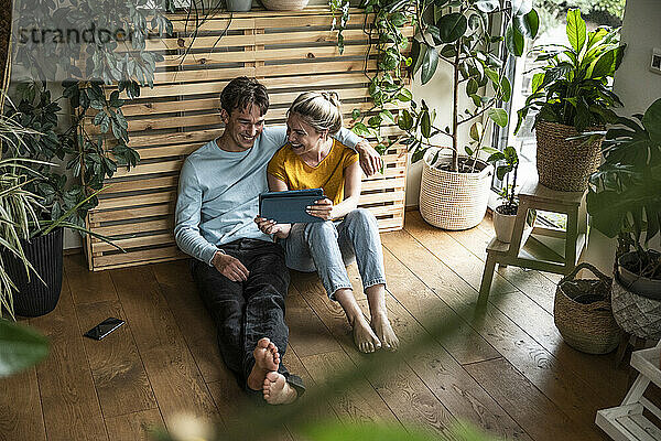 Smiling man with arm around girlfriend holding tablet PC and sitting at home