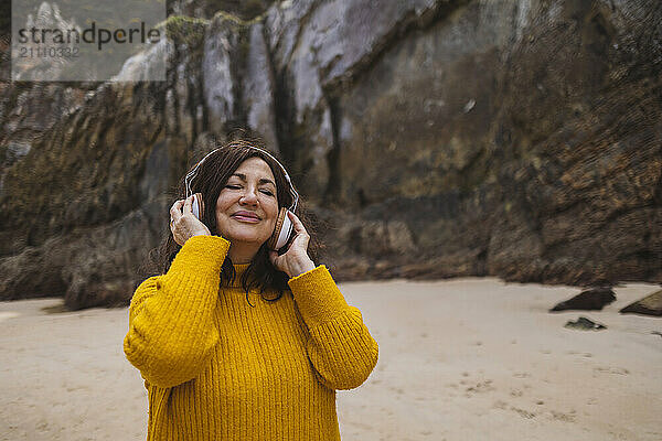 Smiling senior woman with eyes closed listening to music on beach